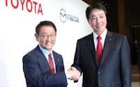 記者会見で握手するトヨタ自動車の豊田社長(左)とマツダの小飼社長（13日午後、東京都港区）
