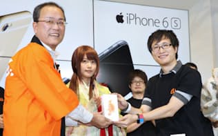 iPhone6sプラスを購入し、KDDIの田中社長（左）から手渡される購入者（25日午前、東京都新宿区）