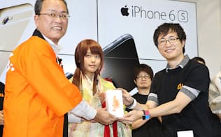 iPhone6sプラスを購入し、KDDIの田中社長(左)から受け取る1番目の購入者（9月25日、東京都新宿区）