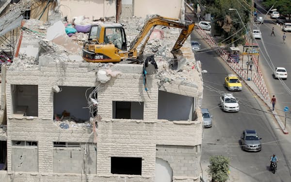 イスラエル軍の空爆を受けたビルの上で、がれきを取り除いている機械（ガザ、25日）=ロイター
