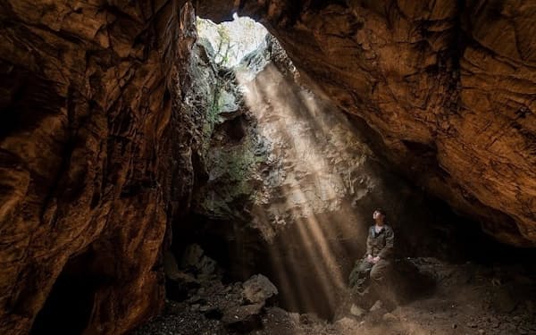 南アフリカのライジング・スター洞窟系の入り口に座る人類学者マリーナ・エリオット氏。同氏のチームは、この洞窟の曲がりくねったトンネル網の奥にある通路で、新たな遺骨を発見した（PHOTOGRAPH BY ROBERT CLARK）
