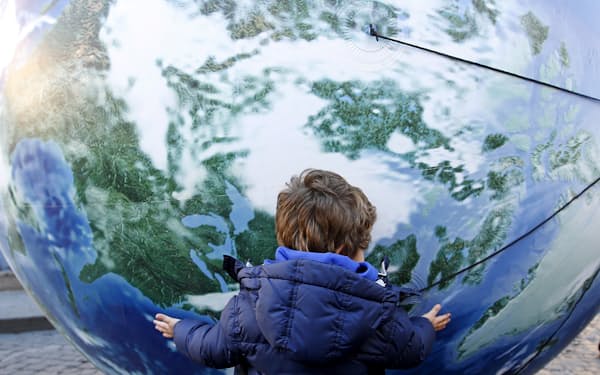 脱炭素が求められるなか運用業界にも厳しい視線が向けられる（地球儀の風船を抱く子ども、イタリア）＝ロイター