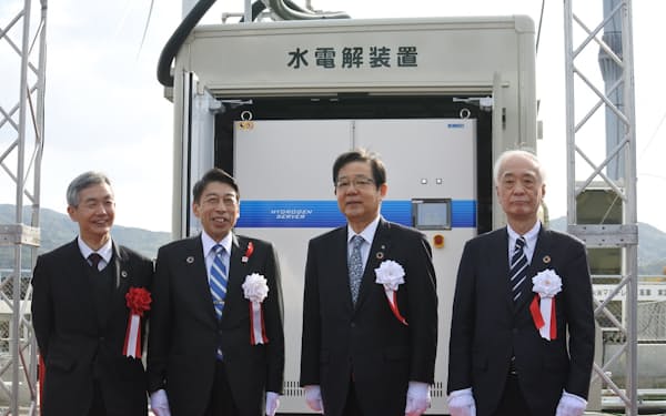 稼働した水素の製造装置の前に立つ福岡県の服部知事（左から2人目）ら（25日、北九州市）