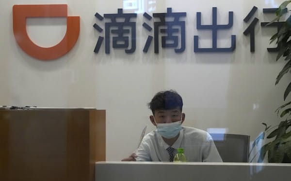 A receptionist looks up near the logo for Didi at an office in Beijing on July 16, 2021. Chinese ride-hailing service Didi Global Inc. said Friday, Dec. 3, 2021 it will pull out of the U.S. stock market and shift its listing to Hong Kong as the ruling Communist Party tightens control over tech industries. (AP Photo/Ng Han Guan)