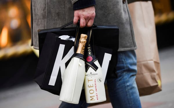 ショッピングバッグとスパークリングワインの瓶を提げた男性（ベルリン、12月）＝ロイター