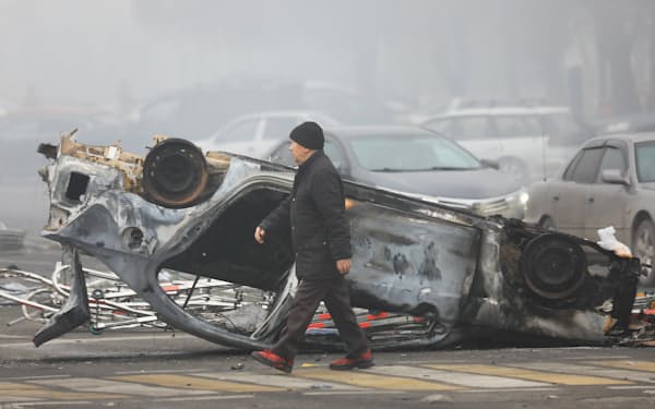抗議デモに関連して焼かれた自動車のそばを歩くカザフスタンの市民（6日、アルマトイ）＝ロイター