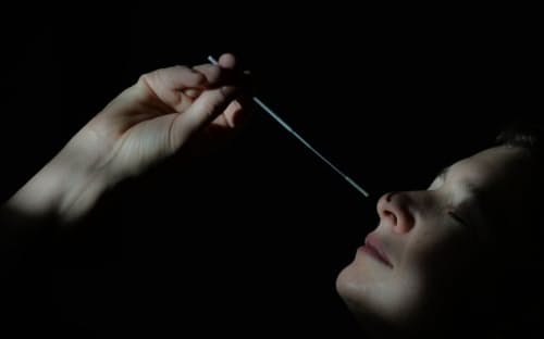 2021年1月6日、カナダのアルバータ州エドモントンで、新型コロナウイルスの迅速抗原検査のために綿棒で検体を採取する女性。オミクロン型では鼻腔ではなく咽頭をぬぐうよう勧める投稿が米国のSNS上で増えているが、抗原検査の使い方は変わるのだろうか。（PHOTOGRAPH BY ARTUR WIDAK, NURPHOTO VIA GETTY IMAGES）