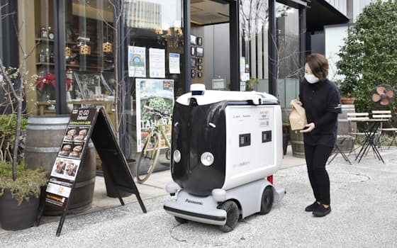 三菱地所の実証実験で、弁当を配達ロボットに入れる店員（25日、東京・大手町）=共同