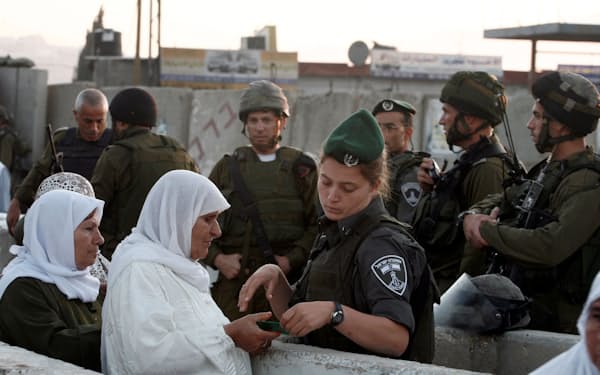 ヨルダン川西岸のラマラ郊外で、エルサレムに入ろうとするパレスチナ人女性を調べるイスラエルの警察官（2011年8月）＝ロイター