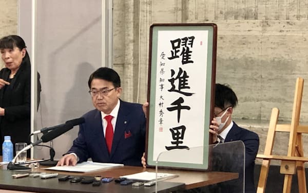 愛知県の大村秀章知事は直筆の書を掲げて県予算案の狙いを説明した（9日、名古屋市の愛知県庁）