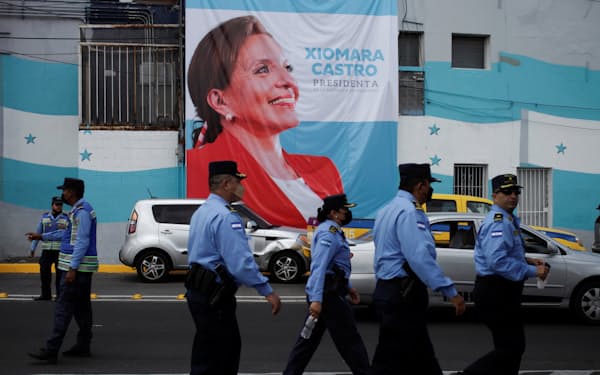 カストロ大統領のポスターの前を歩くホンジュラスの警官たち＝ロイター