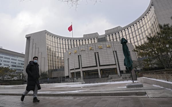 A man wearing a face mask to protect from the coronavirus walks by China's central bank in Beijing, Thursday, Jan. 20, 2022. The Chinese central bank cut rates on one- and five-year loans after growth in the world's second-largest economy sank to 4% over a year earlier in the latest quarter following a crackdown on surging debt among real estate developers. (AP Photo/Andy Wong)