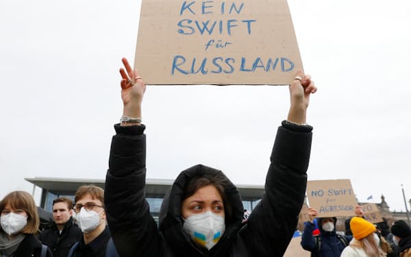 2月25日、ベルリンで開かれたロシアのウクライナ侵略に対する抗議集会で「ロシアをＳＷＩＦＴから排除しろ」と書いたポスターを掲げる参加者＝ロイター