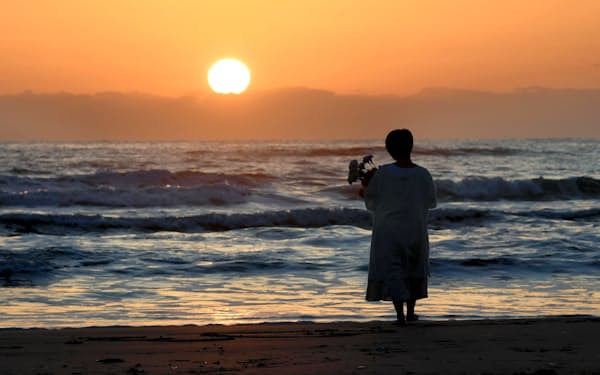 震災から10年目を迎えた11日、いわき市にある海辺を朝日が照らす中、花束をもつ女性が海に向かって祈っていた（11日午前、福島県いわき市）