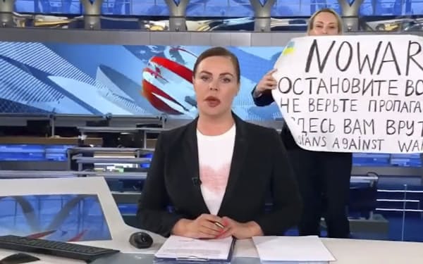 ロシアのテレビの生放送中にキャスターの背後で「戦争をやめて」などと書いた紙を掲げる女性（ウクライナのポドリャク大統領府長官顧問のツイッターから）＝共同