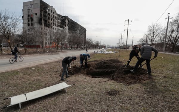 犠牲者を埋葬するための穴を掘る人々（２０日、ウクライナ南東部マリウポリ）＝ロイター