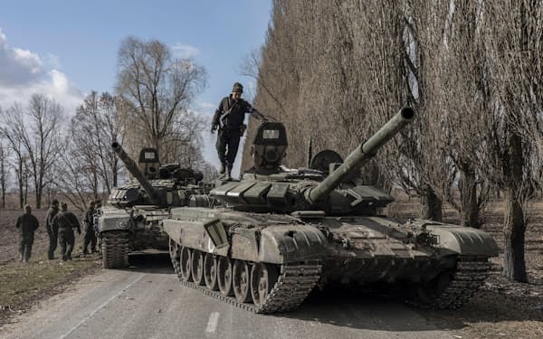 ロシア軍から奪った戦車の上に立つウクライナ兵（27日、キーウ郊外）＝ロイター