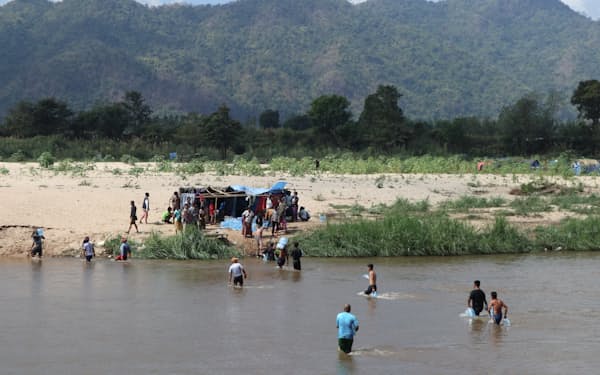 国軍による襲撃を逃れるため、タイとの国境に流れる川を渡って避難するミャンマー人=AP