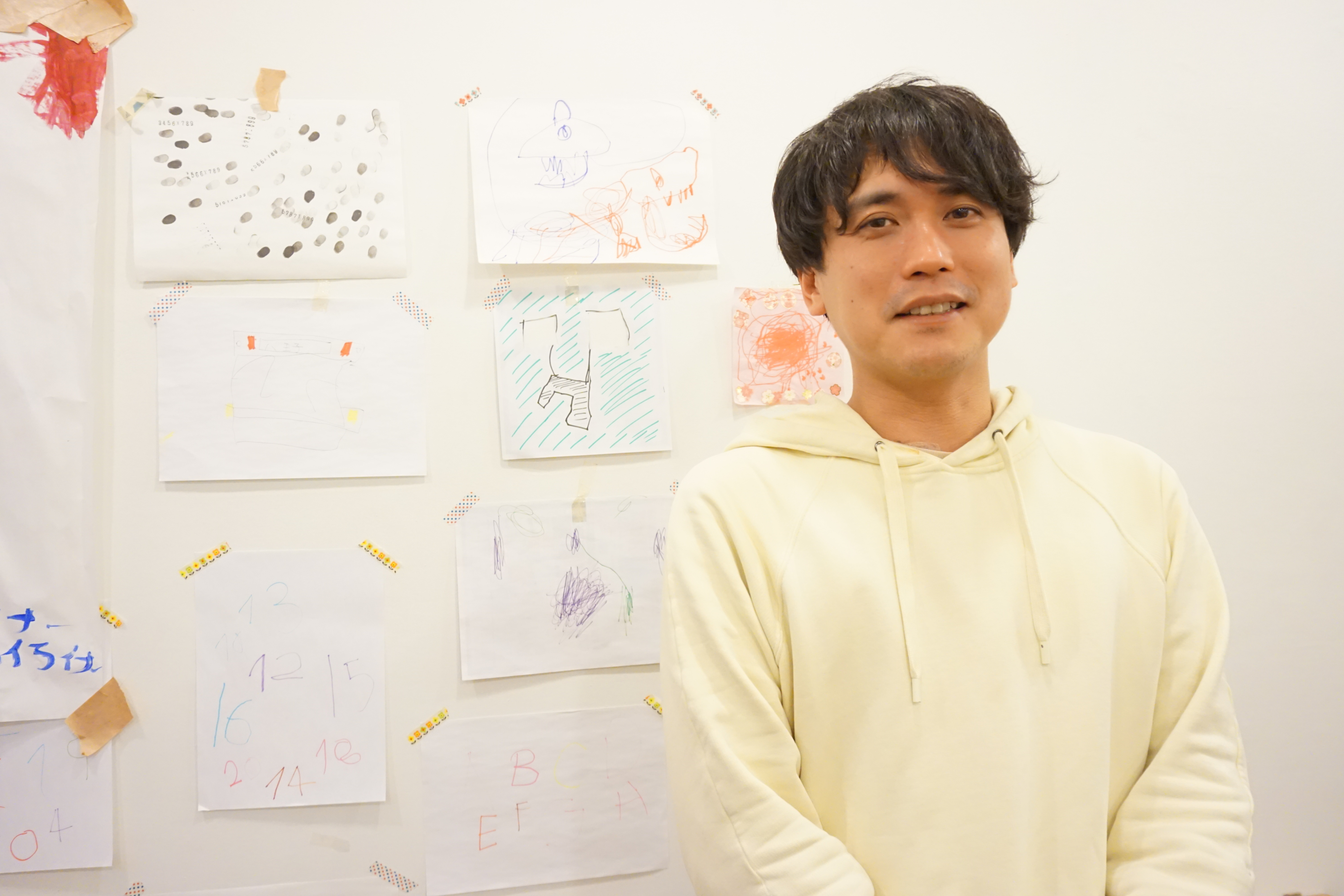 Woody社長の中里祐次氏 背景の壁には子供たちの絵が貼られている