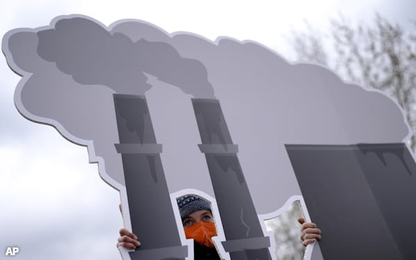 ドイツのベルリンで発電所を描いたプラカードを掲げて化石燃料の利用に反対する人たち=AP