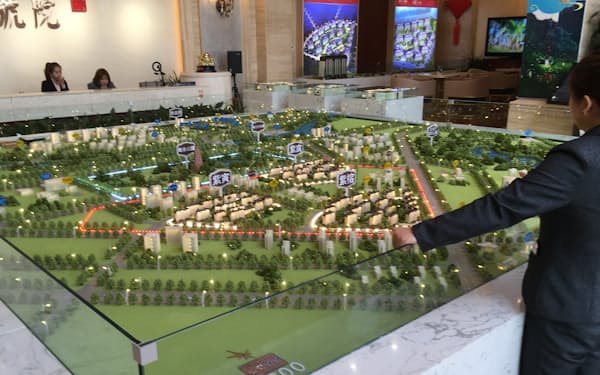 新築マンションエリアの全体像を模型で説明する住宅展示場の販売員（内モンゴル自治区オルドス市）