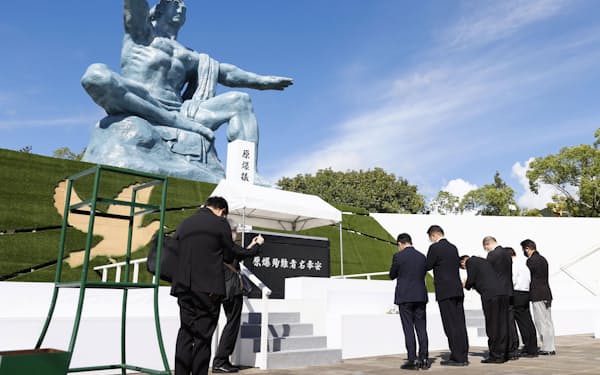 　長崎市の平和公園を訪れ、平和祈念像に手を合わせる人たち=8日午後