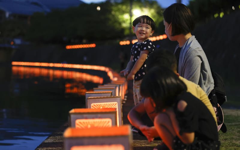 被爆後多くの人が水を求めた浦上川で行われた「万灯流し」で、並べられた灯籠を見つめる親子（9日夜、長崎市）=共同