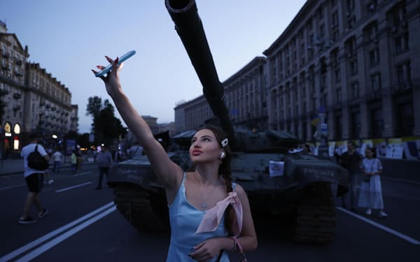 ウクライナの首都キーウ中心部の大通りに展示されたロシア軍の戦車前で記念撮影する女性＝23日夜（共同）