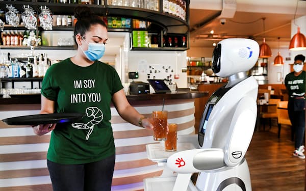 新型コロナの感染対策として導入された給仕ロボットに飲み物を手渡すウエートレス＝ロイター