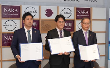 サインした協定書を掲げる奈良県の山下知事(中)ら(16日、奈良市)