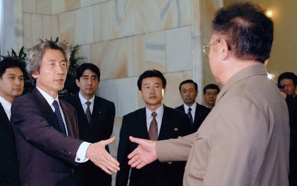 2002年9月、平壌市内の百花園迎賓館で握手を求めて歩み寄る小泉純一郎首相（左）と北朝鮮の金正日総書記。左から3人目は安倍晋三官房副長官＝共同