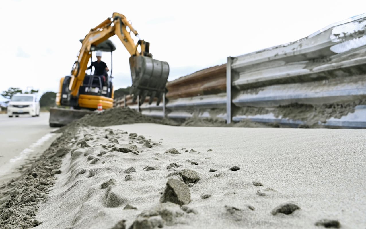 台風14号の影響で海岸沿いの道路にあふれた砂。撤去作業が行われていた（20日午前、徳島県鳴門市）=共同