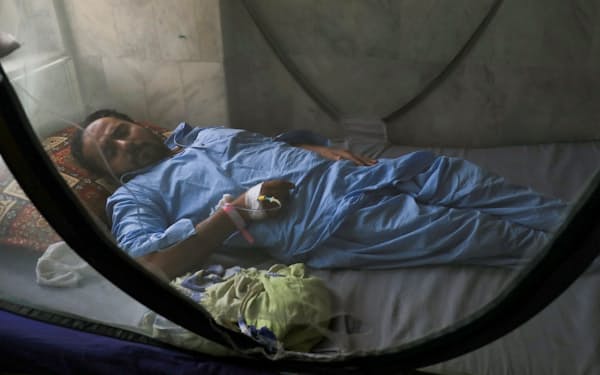 蚊帳の中で横たわるデング熱患者。デング熱も後遺症が知られている（パキスタン）＝ロイター