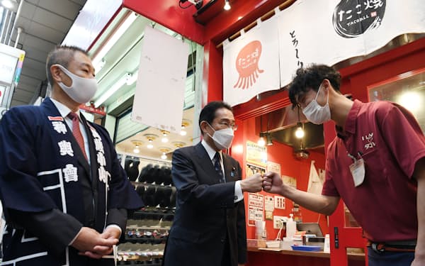商店街の視察で、たこ焼き店の店主（右）と拳を合わせる岸田首相（15日、東京都品川区）