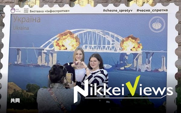 8日、ロシア本土と結ぶクリミア橋の崩落を受け、ウクライナの首都キーウ市内に登場した切手風の絵画の前で記念撮影する市民=
                                                        共同