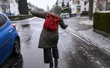 通勤中の女性。ブラックアイスバーンで滑らないよう、凍った路面でバランスを取ろうとしている。ブラックアイスバーンは車だけでなく歩行者にとっても危険だ。(UWE ZUCCHI, PICTURE ALLIANCE, GETTY IMAGES)
