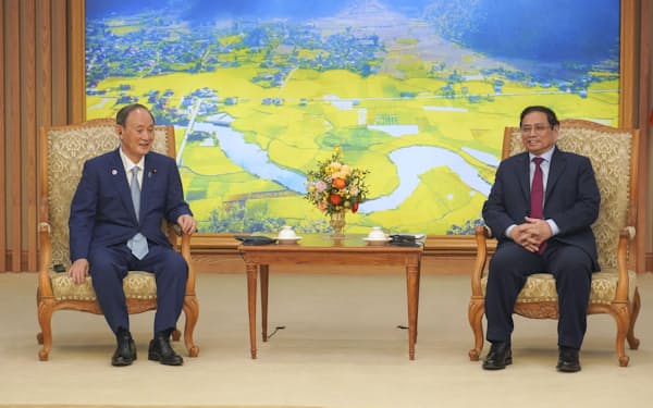 9日、ベトナムの首都ハノイでファム・ミン・チン首相（右）と会談する菅義偉前首相（共同）