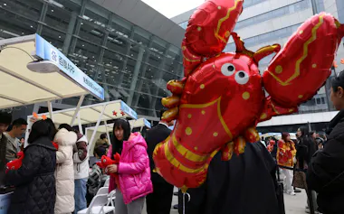 中国で開かれたOpenClawの関連イベントは多くの人でにぎわった(写真中央はOpenClawのロゴマークのキャラクターであるロブスター、17日、北京市)=ロイター