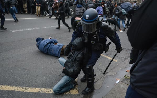 19日、フランス・パリで、政府の年金制度改革案に反対するデモ参加者を拘束する警官（ゲッティ＝共同）