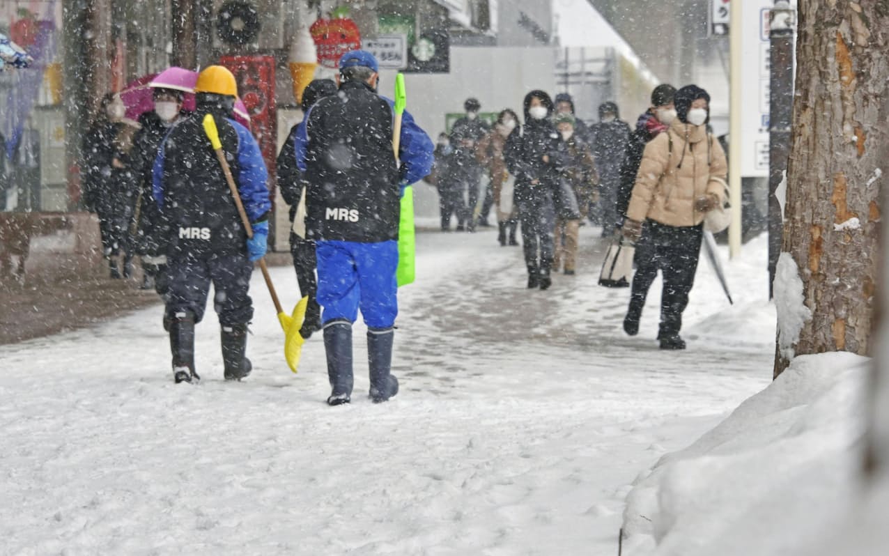 降雪の中、青森駅前を行き交う人たち（24日午前、青森市）=共同