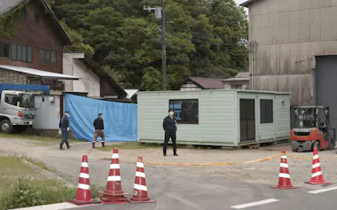 男性の遺体が土の中に埋められているのが見つかった現場周辺を警戒する広島県警の捜査員ら(29日、広島県三原市)=共同