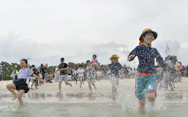 和歌山県白浜町の白良浜が海開きし、海へ駆け込む海水浴客(3日)=共同