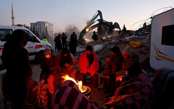 13日、たき火で暖を取る被災者ら（トルコ南部カフラマンマラシュ県）＝ロイター