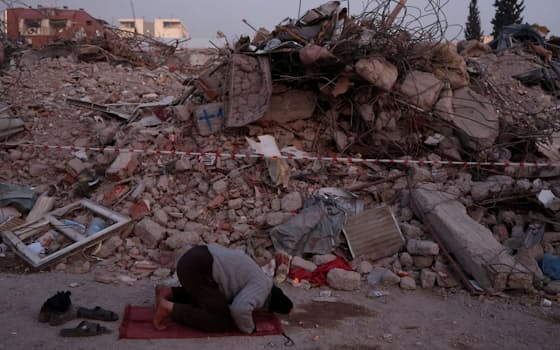 崩れ落ちた家屋の前で祈る男性（14日、トルコ南部カフラマンマラシュ県）=ロイター
