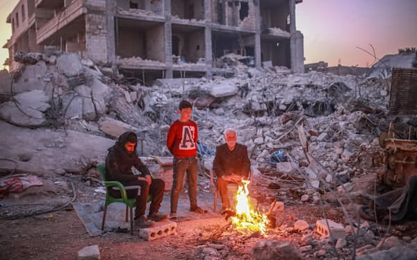 シリア北部アレッポの壊れた建物の近くで暖を取る人たち（18日）＝ゲッティ共同