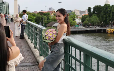 「メモリアルブリッジ」でハスの花束を手に写真撮影する女性(12日、バンコク)=小林健撮影