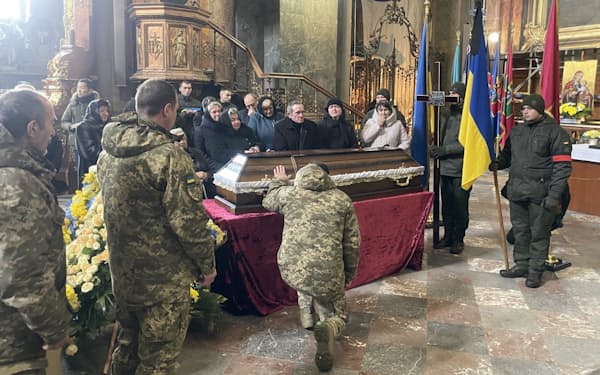 ひつぎに手をかけ祈りをささげるウクライナ軍の兵士（21日、リビウの聖ペテロ・パウロ教会）＝林英樹撮影