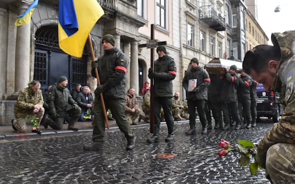 戦死者の葬列にひざまずくウクライナ兵（21日、リビウ）