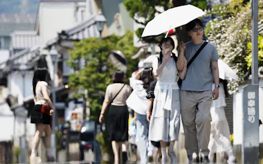 今年全国で初めての猛暑日となった大分県日田市で、かげろうが立つ中を歩く人たち(18日)=共同
