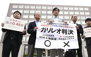 衆院選の「1票の格差」訴訟の判決を受け、札幌高裁前で「ガリレオ判決」などと書かれた紙を掲げる原告側の伊藤真弁護士(中央)ら(29日)=共同